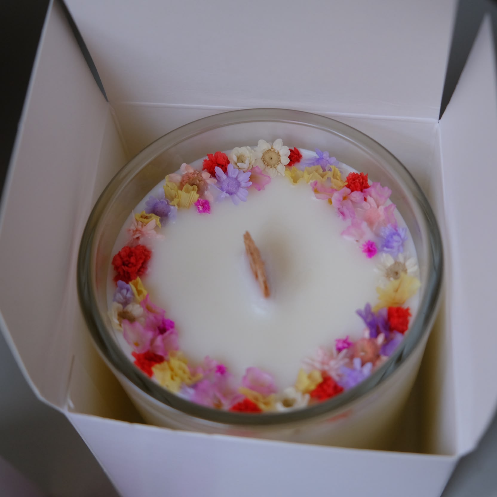 Geöffnete Geschenkbox mit einer blumenverzierten Kerze darin
