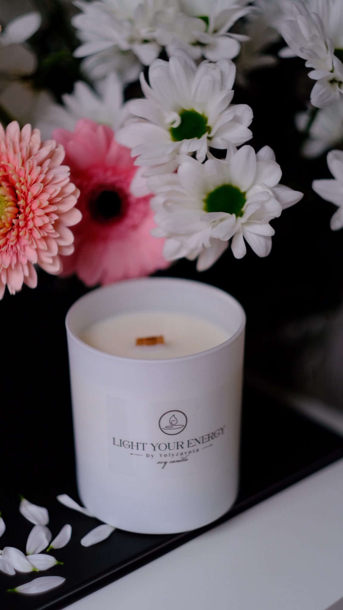 Light Your Energy Kerze mit Blütendekor, umgeben von rosa und weissen Blumen